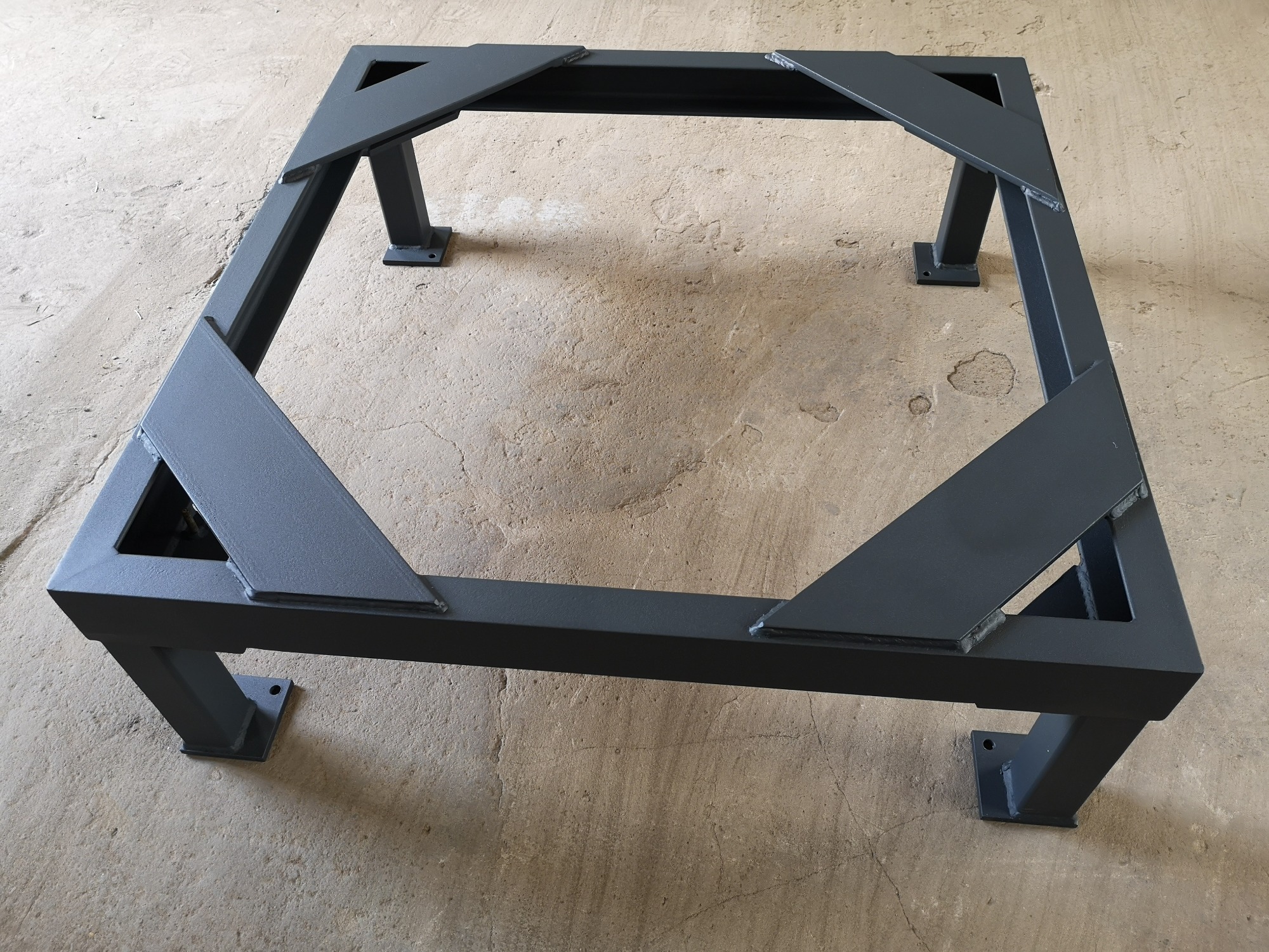 Metalowa konstrukcja spawana z profili kwadratowych, pomalowana na szaro, z widocznymi spawami, stojąca na betonowej posadzce.