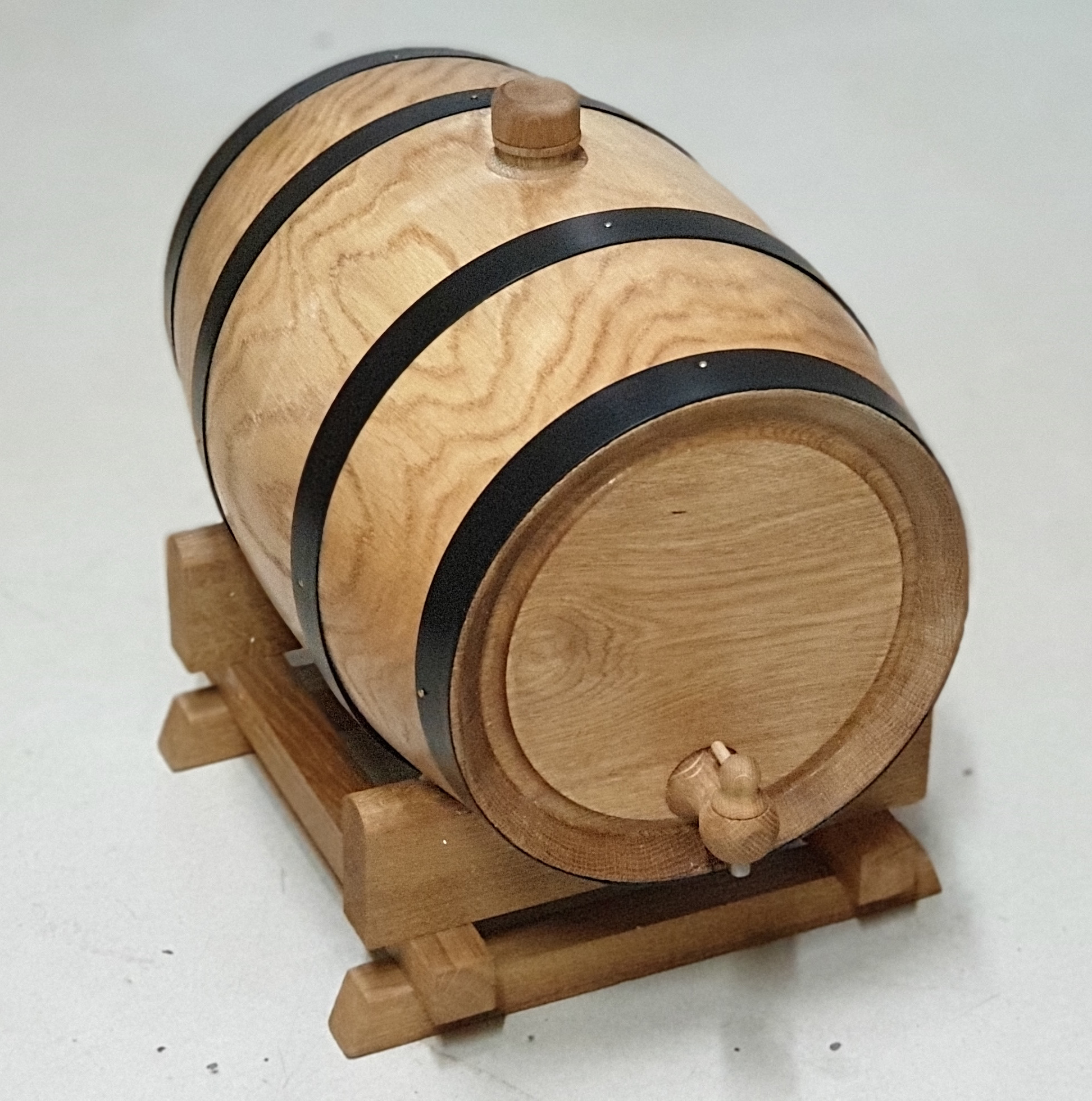 Drewniana beczka z czarnymi obręczami, kranikiem i drewnianą podstawką na jasnym tle.