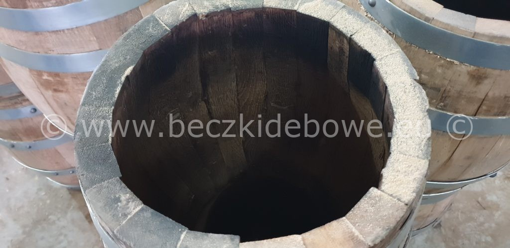 Wnętrze dębowej beczki z metalowymi obręczami, widoczne słoje drewna i jasny osad na krawędziach.