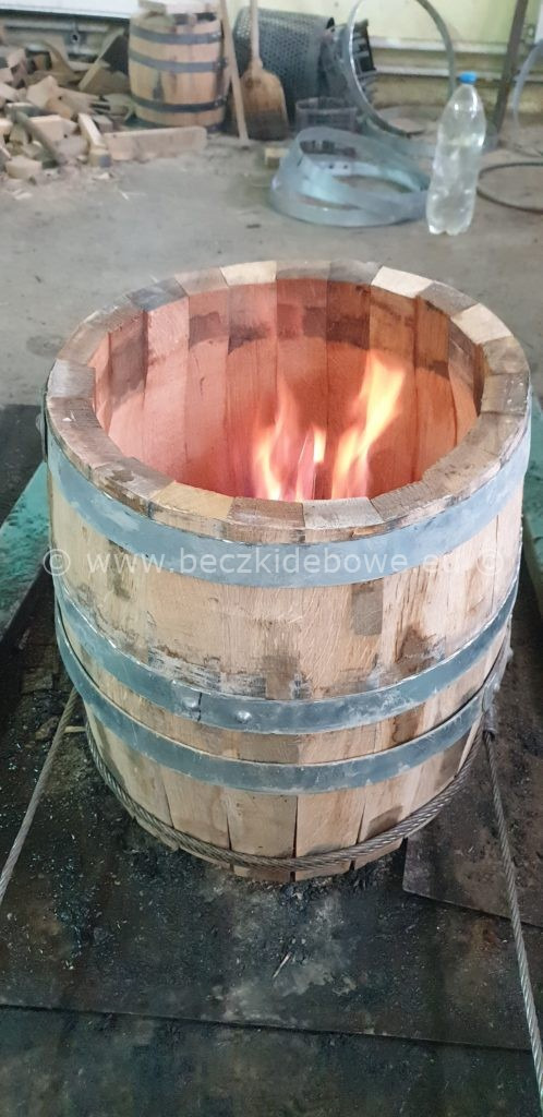 Wnętrze dębowej beczki opalane ogniem podczas procesu produkcyjnego, widoczne metalowe obręcze i drewniane klepki.