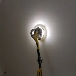 Szlifierka do gładzi na wysięgniku z oświetleniem LED w trakcie pracy na ścianie pod skosem poddasza.