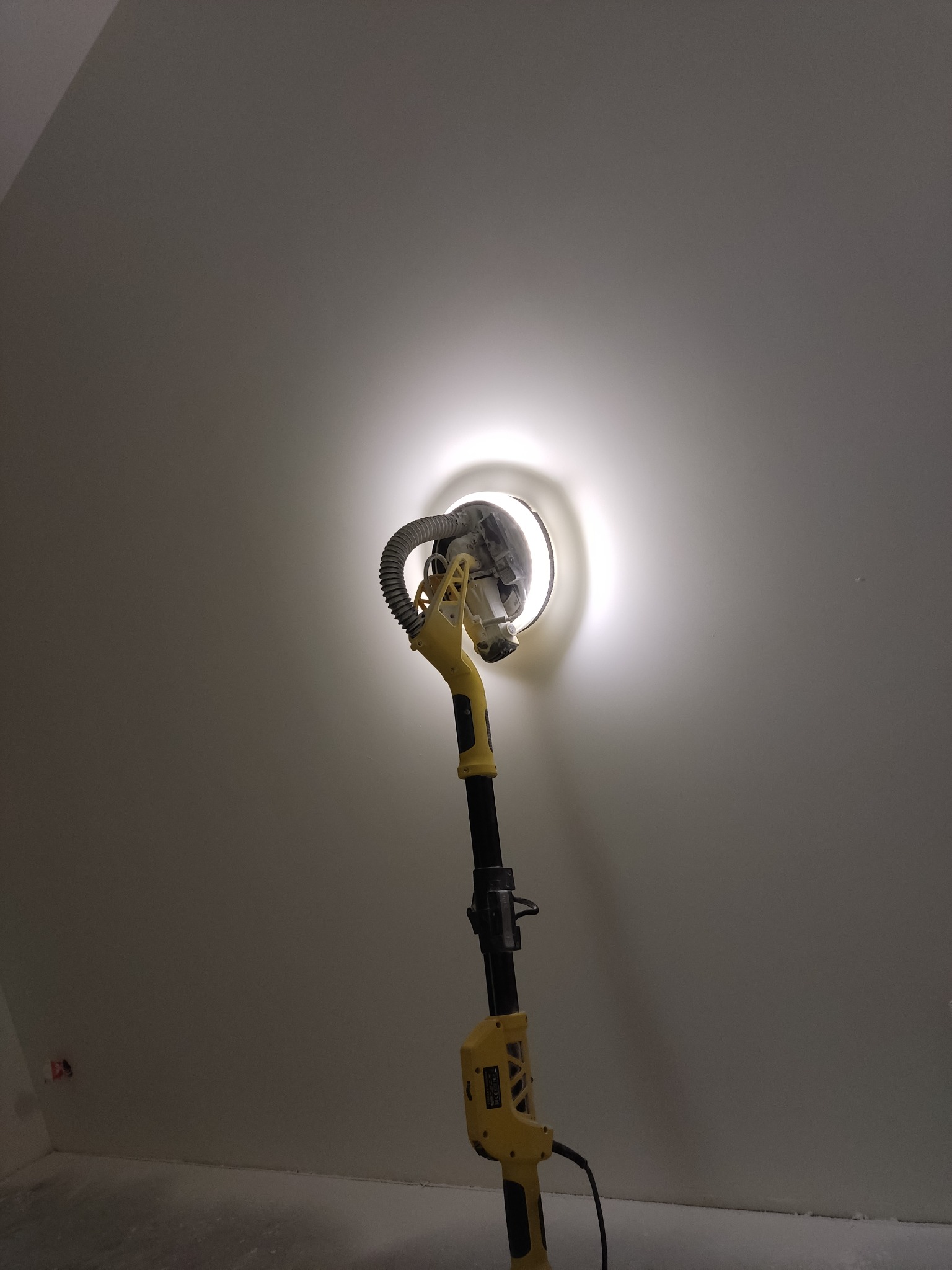 Szlifierka do gładzi na wysięgniku z oświetleniem LED w trakcie pracy na ścianie pod skosem poddasza.