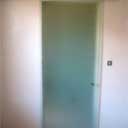 Matowa szklana tafla w ramie, prawdopodobnie drzwi lub ścianka działowa, widoczna klamka i włącznik światła na ścianie obok.