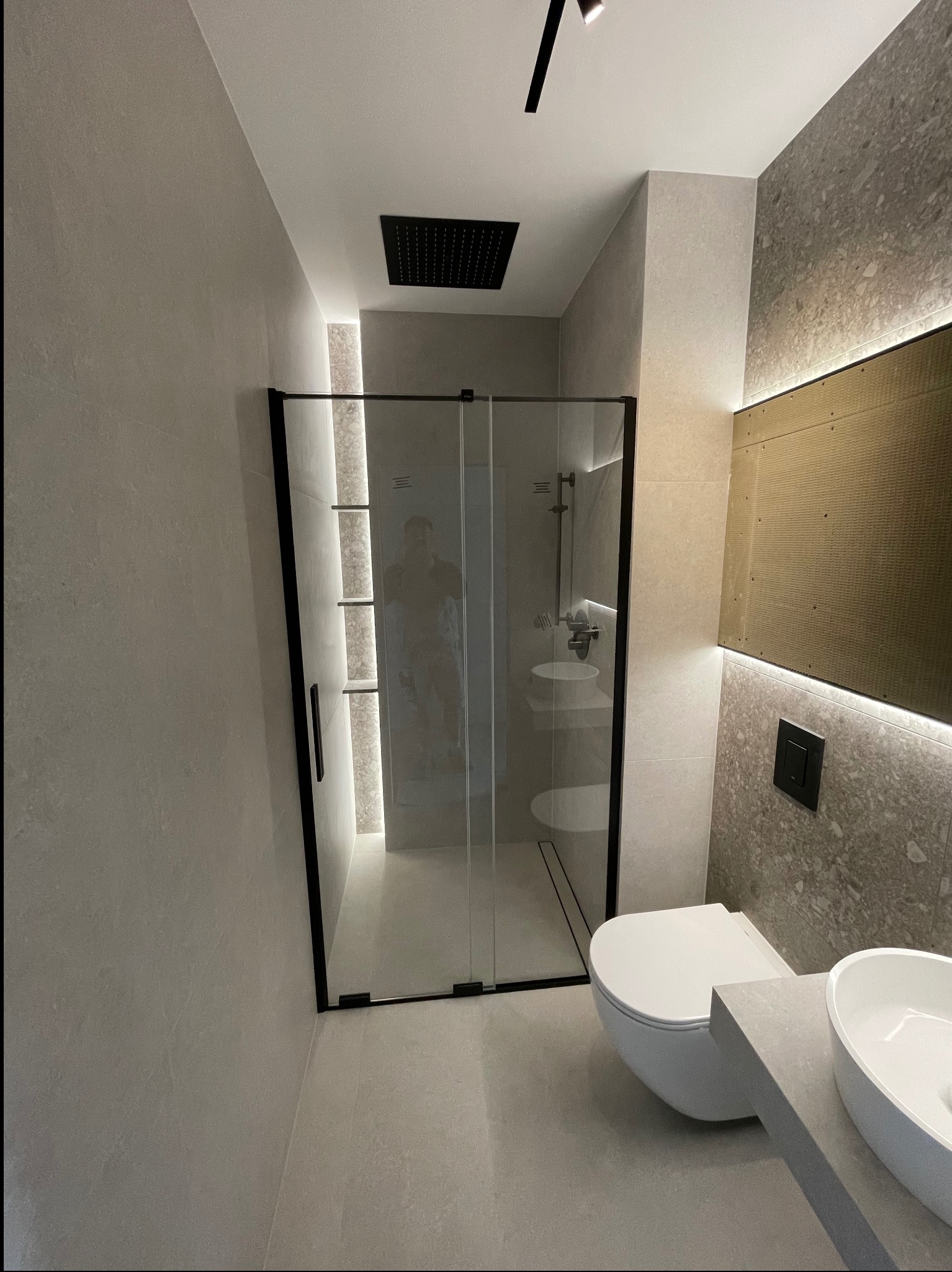 Nowoczesna łazienka z kabiną prysznicową typu walk-in z czarnymi ramami, podświetlanym lustrem i umywalką nablatową na szarym blacie.