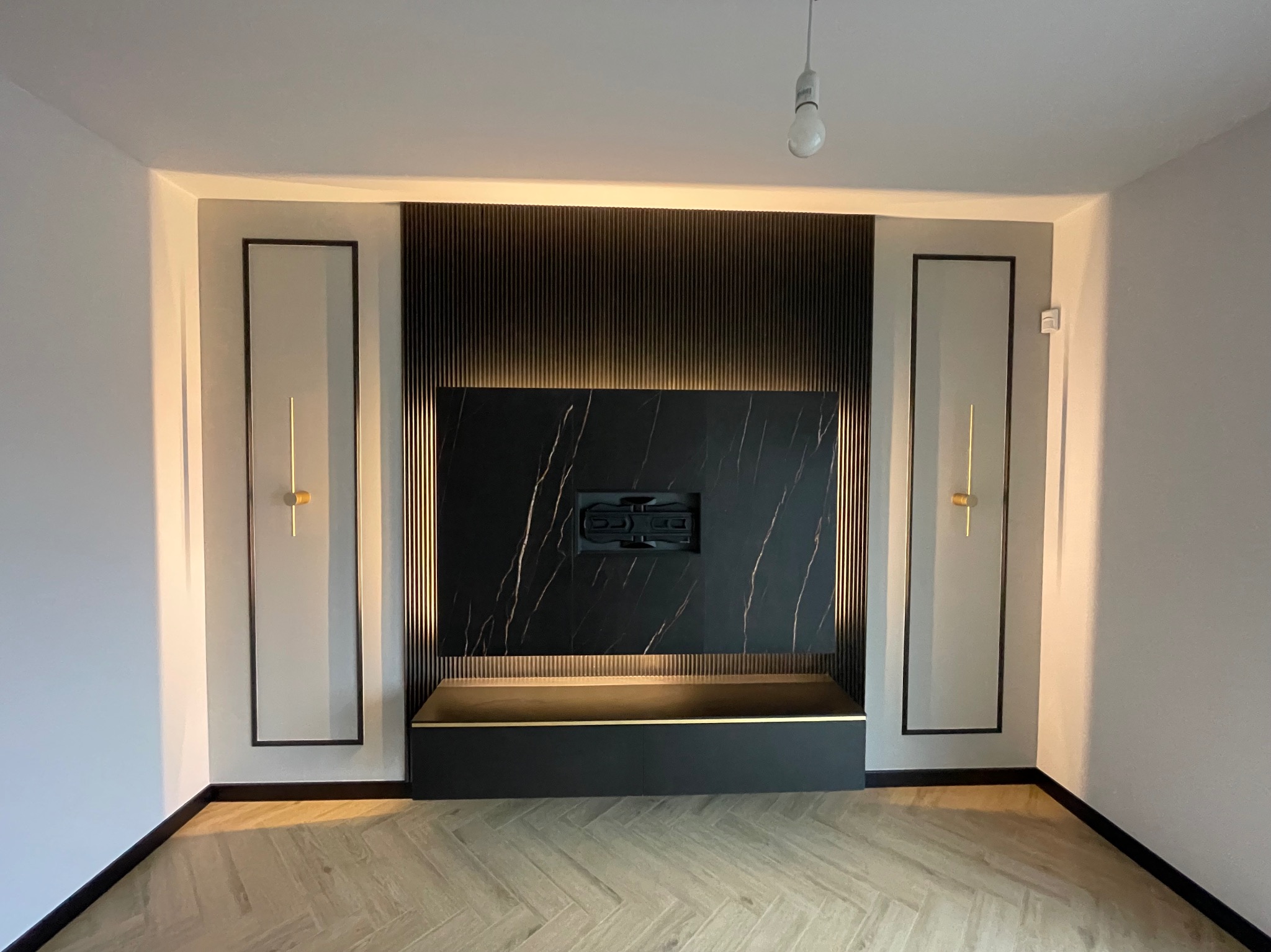 Eleganckie wykończenie ściany z czarnym marmurem, ryflowanymi panelami i oświetleniem LED. Na podłodze parkiet w jodełkę. Minimalistyczny design wnętrza.