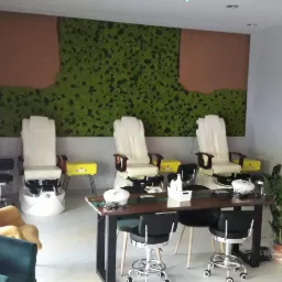 Jasne wnętrze salonu kosmetycznego z trzema fotelami do pedicure, stolikami do manicure, ścianą z mchu i brązowymi panelami, oraz elementami dekoracyjnymi.