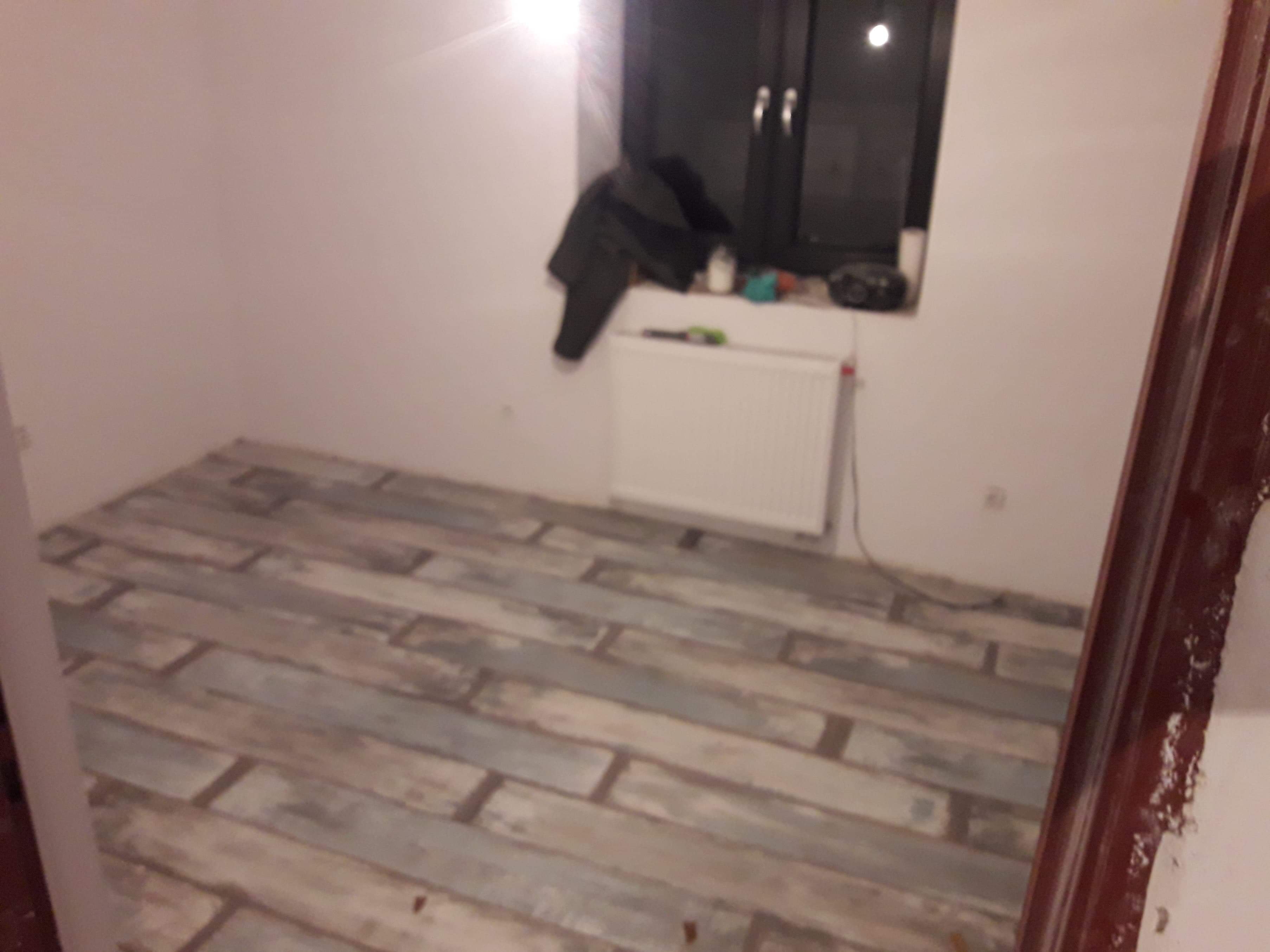 Ułożony parkiet w pokoju z grzejnikiem pod oknem, widoczne niedociągnięcia przy ścianach i brak listew przypodłogowych.