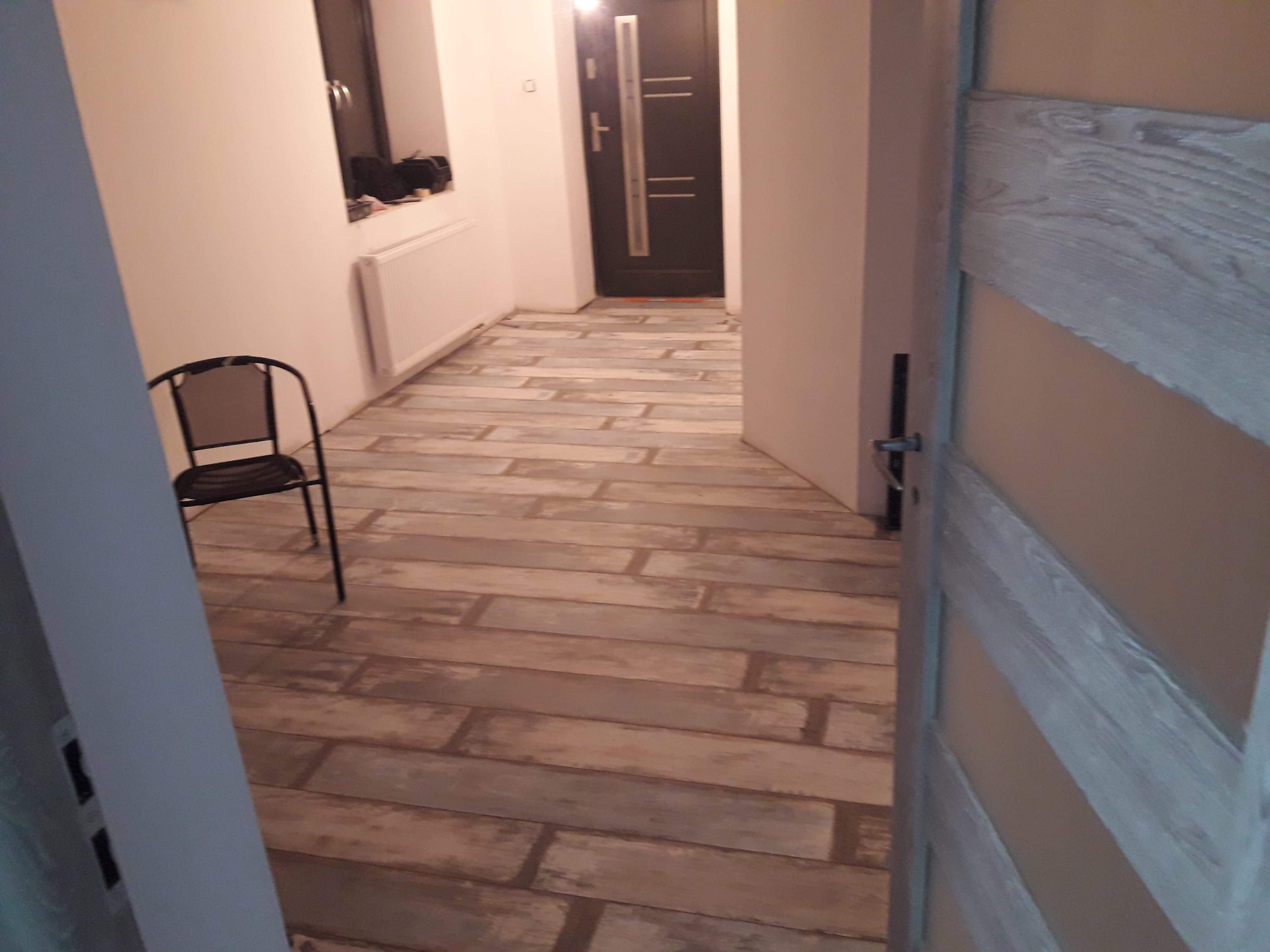 Ułożony parkiet panelowy w odcieniach szarości i brązu w korytarzu w Czudcu, widok na drzwi wejściowe i krzesło.