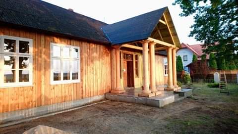 Odnowiony drewniany dom z kolumnami przy wejściu, widoczne świeżo pomalowane ściany i fundament, teren wokół domu jeszcze niezagospodarowany.