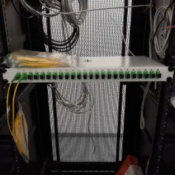 Panel krosowniczy światłowodowy z ponumerowanymi portami w szafie rack, widoczne przewody światłowodowe i kable wewnątrz szafy.