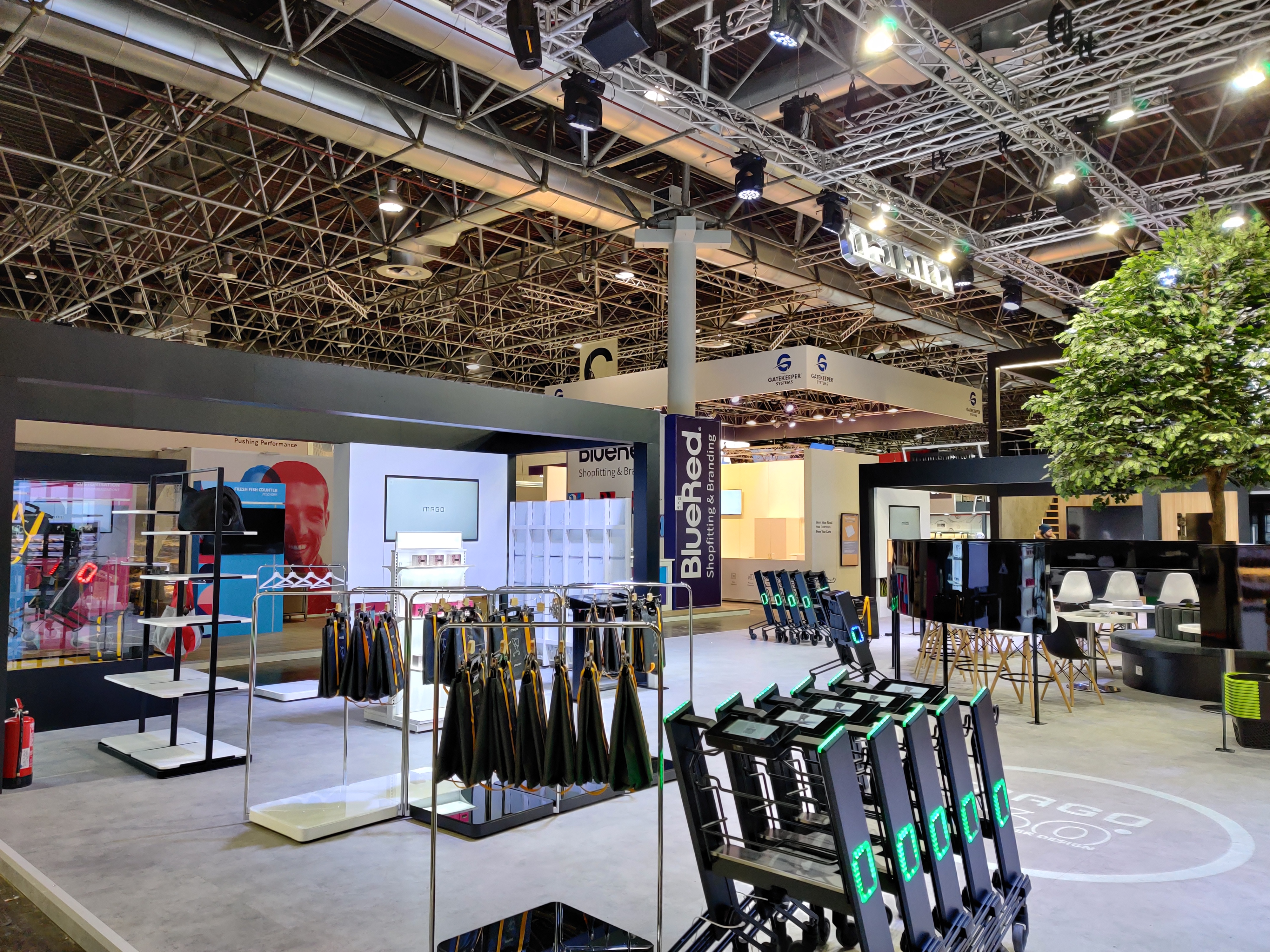 Wnętrze stoiska targowego z ekspozycją wózków sklepowych z wyświetlaczami, regałami i elementami identyfikacji wizualnej firmy.