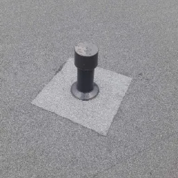 Szary, płaski dach pokryty papą z zamontowanym kominkiem wentylacyjnym z kroplami wody na szczycie.