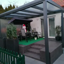 Zadaszony taras z meblami ogrodowymi i dekoracjami świątecznymi w Borkach, widok z zewnątrz przez zielony płotek.