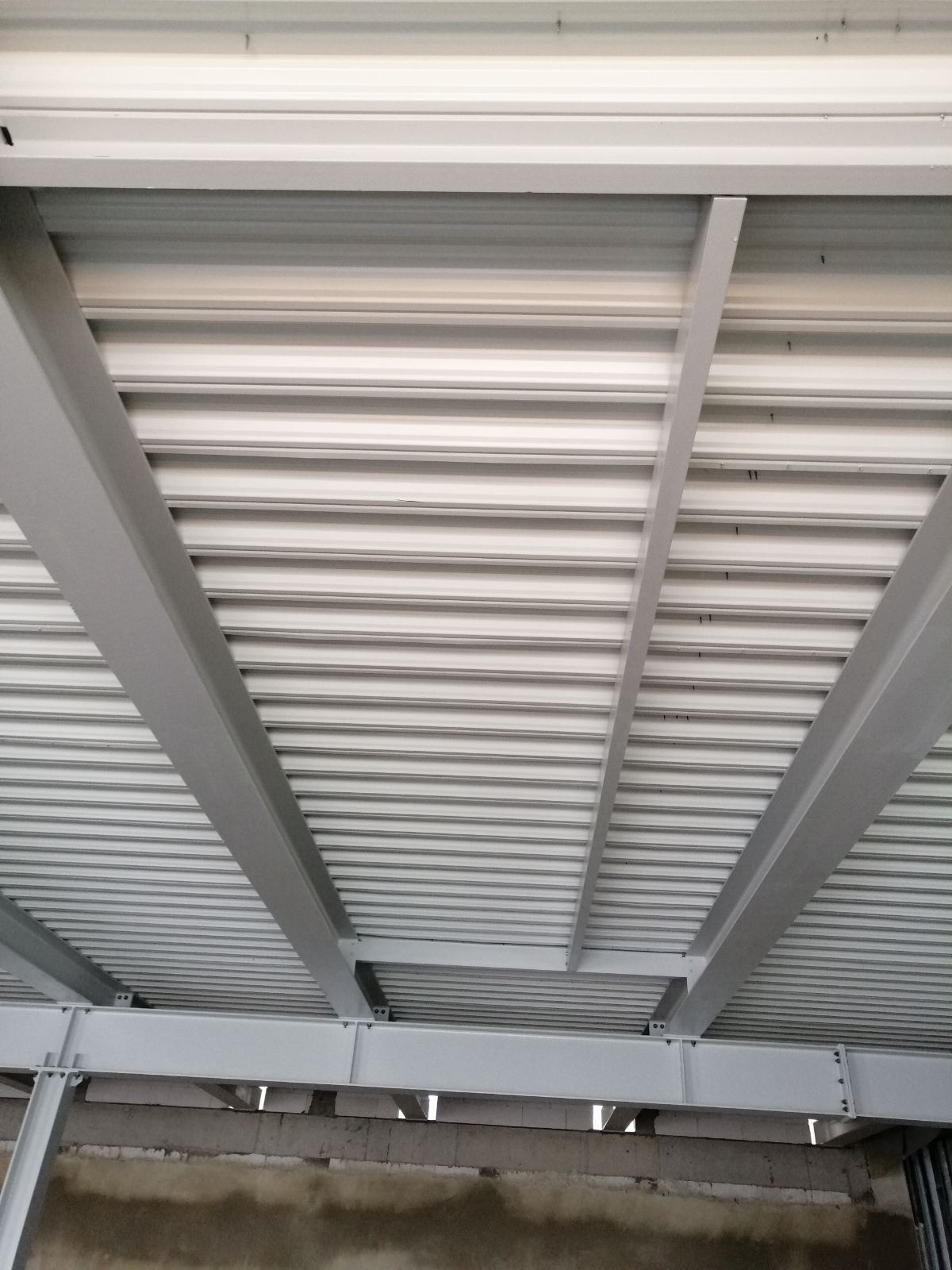 Widok od dołu na konstrukcję dachu z blachy trapezowej i stalowych belek nośnych, widoczne ślady po spawaniu.