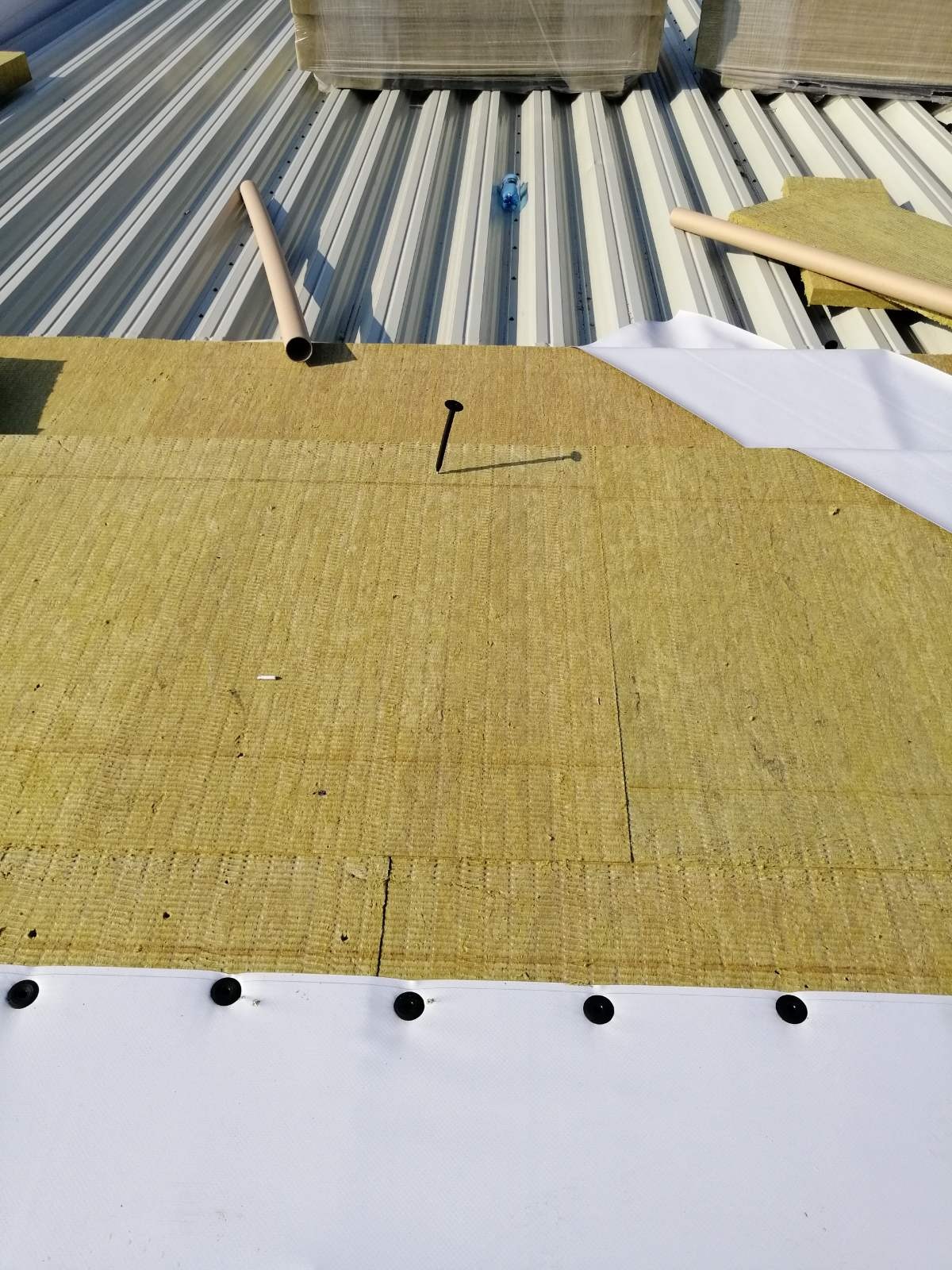 Warstwy izolacji termicznej z wełny mineralnej i membrany dachowej na metalowym dachu, zabezpieczone gwoździem, widok z góry.