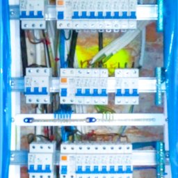 DOM - Artur Cybulski - Rozdzielnia elektryczna z zamontowanymi bezpiecznikami i przewodami, widok z bliska na instalację w skrzynce, zabezpieczona folią malarską.