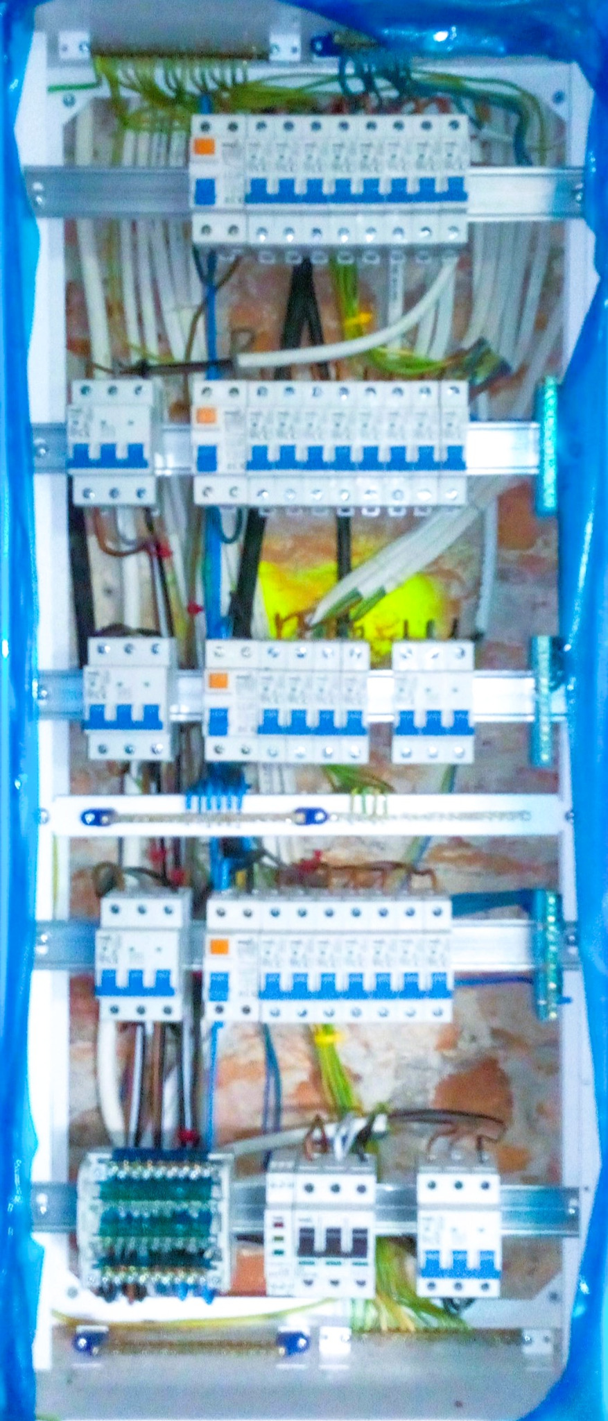 Rozdzielnia elektryczna z zamontowanymi bezpiecznikami i przewodami, widok z bliska na instalację w skrzynce, zabezpieczona folią malarską.