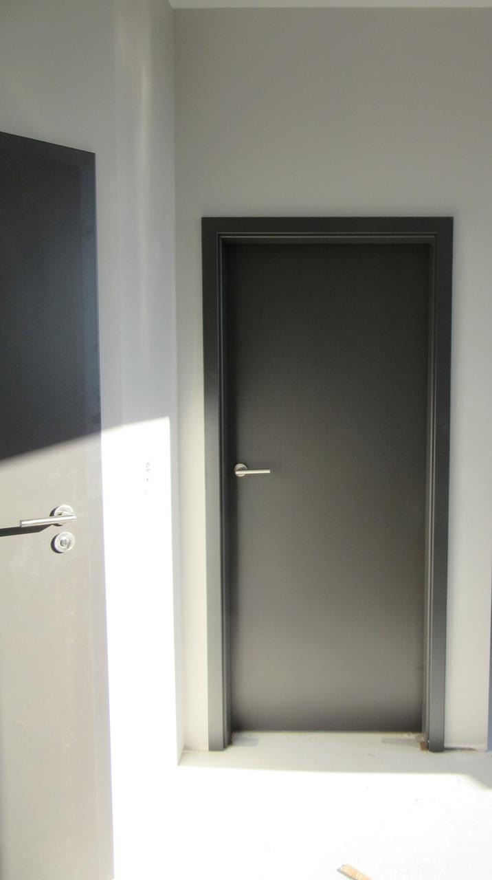 Dwie szare płaskie skrzydła z prostymi srebrnymi klamkami na tle jasnoszarej ściany, jedno zamknięte, drugie uchylone.