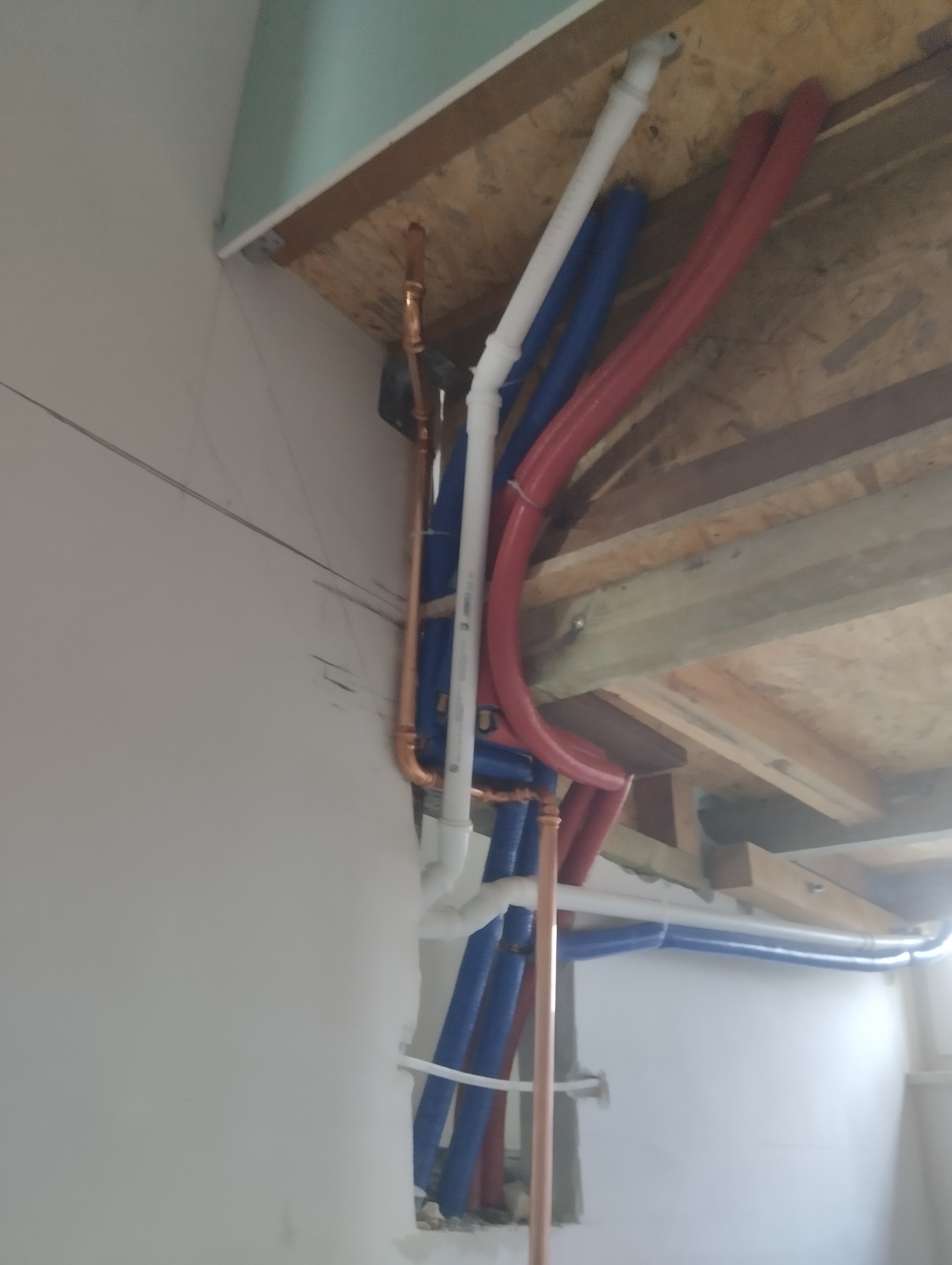 Instalacja rur CO i wodnych (czerwone, niebieskie i białe) w przestrzeni pod stropem, widoczne fragmenty ścian i drewnianej konstrukcji sufitu.