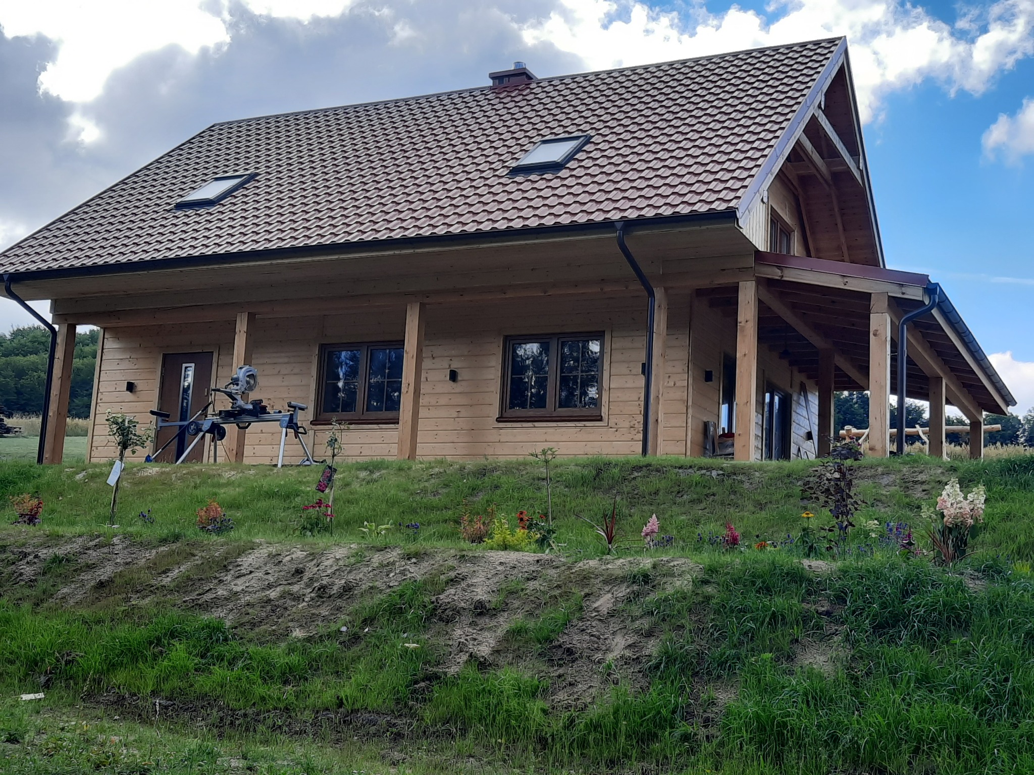 Nowoczesny dom szkieletowy z brązowym dachem i oknami dachowymi, widoczny z poziomu gruntu, z narzędziami budowlanymi na pierwszym planie.