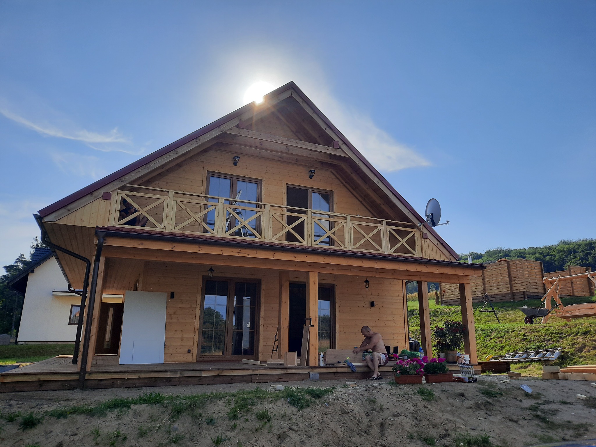 Nowoczesny dom szkieletowy z balkonem w Rumii w trakcie wykończenia, widoczny pracownik na werandzie, jasne drewno, słoneczny dzień.