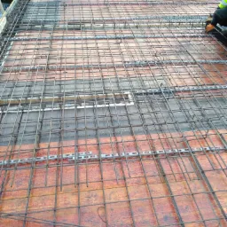 Zbrojenie stropu z siatki stalowej na ceramicznych pustakach, widoczny fragment pracownika w odblaskowej kamizelce.