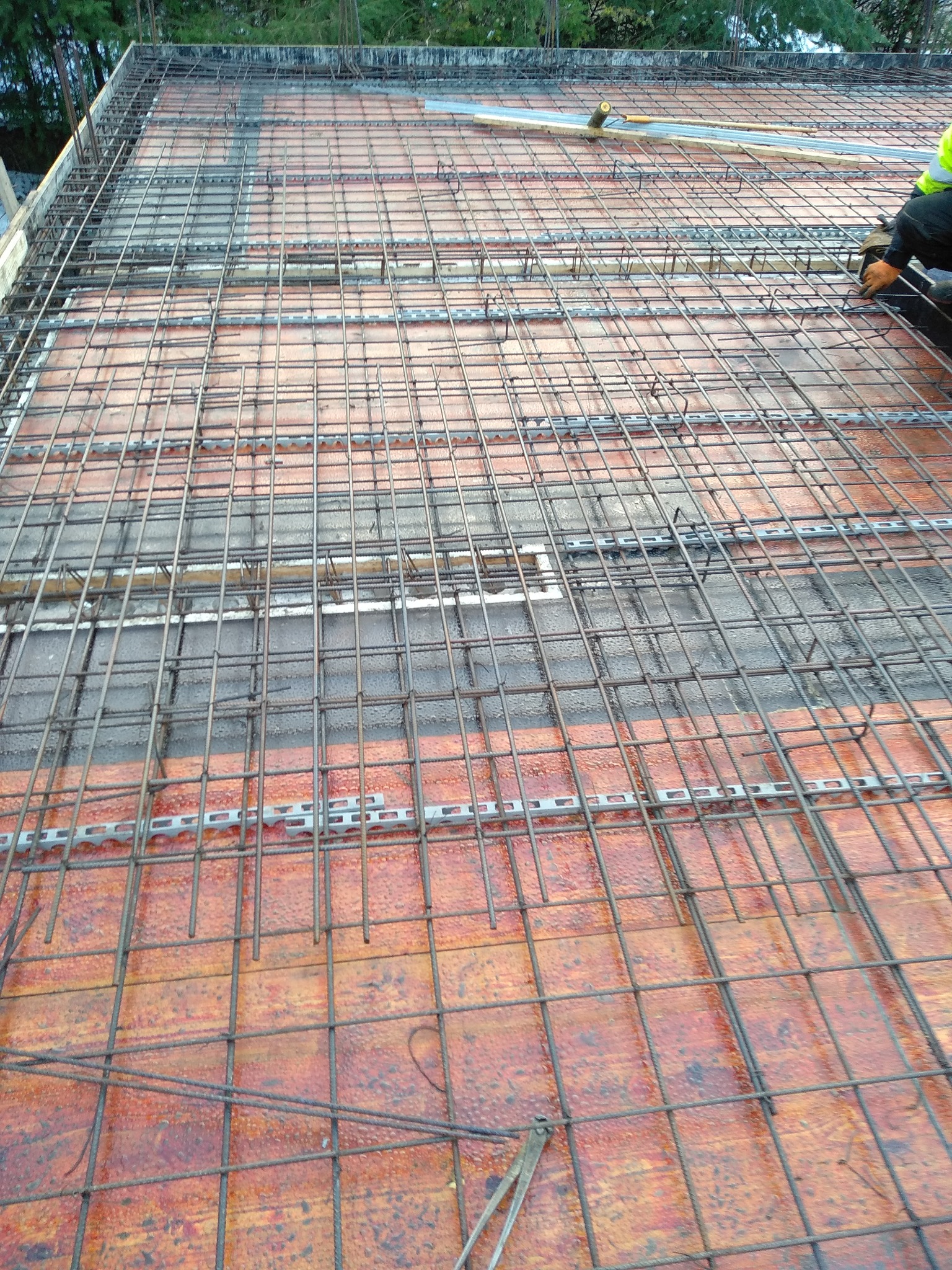 Zbrojenie stropu z siatki stalowej na ceramicznych pustakach, widoczny fragment pracownika w odblaskowej kamizelce.