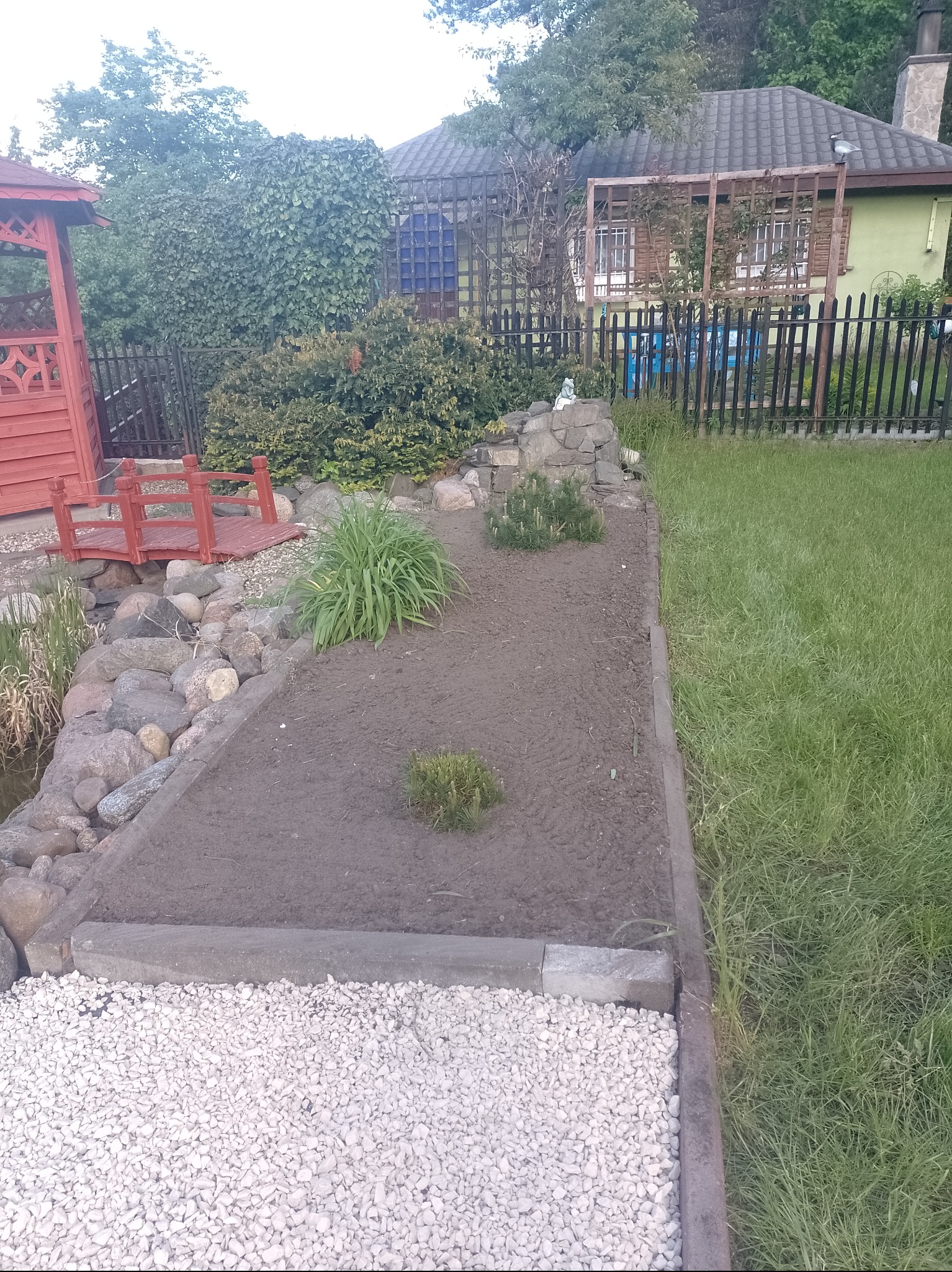 Przygotowany teren pod nasadzenia w ogrodzie z elementami skalniaka, widoczny fragment trawnika i mała architektura ogrodowa.