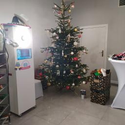 Sebastian Kołodziejczyk Tiases Taxi - Fotobudka z ekranem dotykowym i rekwizytami w świątecznej scenerii z choinką, pudełkami prezentowymi i stolikiem z przebraniami.