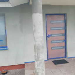 Elewacja domu w trakcie tynkowania, okno i drzwi zabezpieczone folią, kolumna w siatce, widoczna miska psa.