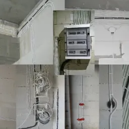 Rozbudowana instalacja elektryczna w budynku w stanie surowym: białe rurki prowadzące przewody, rozdzielnia elektryczna na ścianie z betonu komórkowego.