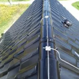 Czarny dach z dach&oacute;wki ceramicznej z zamontowaną instalacją odgromową, widok z g&oacute;ry w słoneczny dzień.