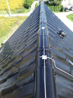 Czarny dach z dachówki ceramicznej z zamontowaną instalacją odgromową, widok z góry w słoneczny dzień.