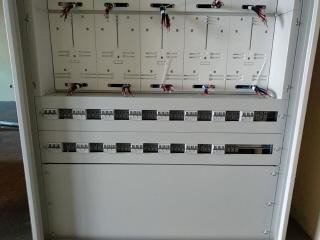 Otwarta, szara skrzynka elektryczna z widocznymi bezpiecznikami, przewodami i elementami montażowymi, sfotografowana z bliska, ukazująca wnętrze rozdzielnicy elektrycznej.