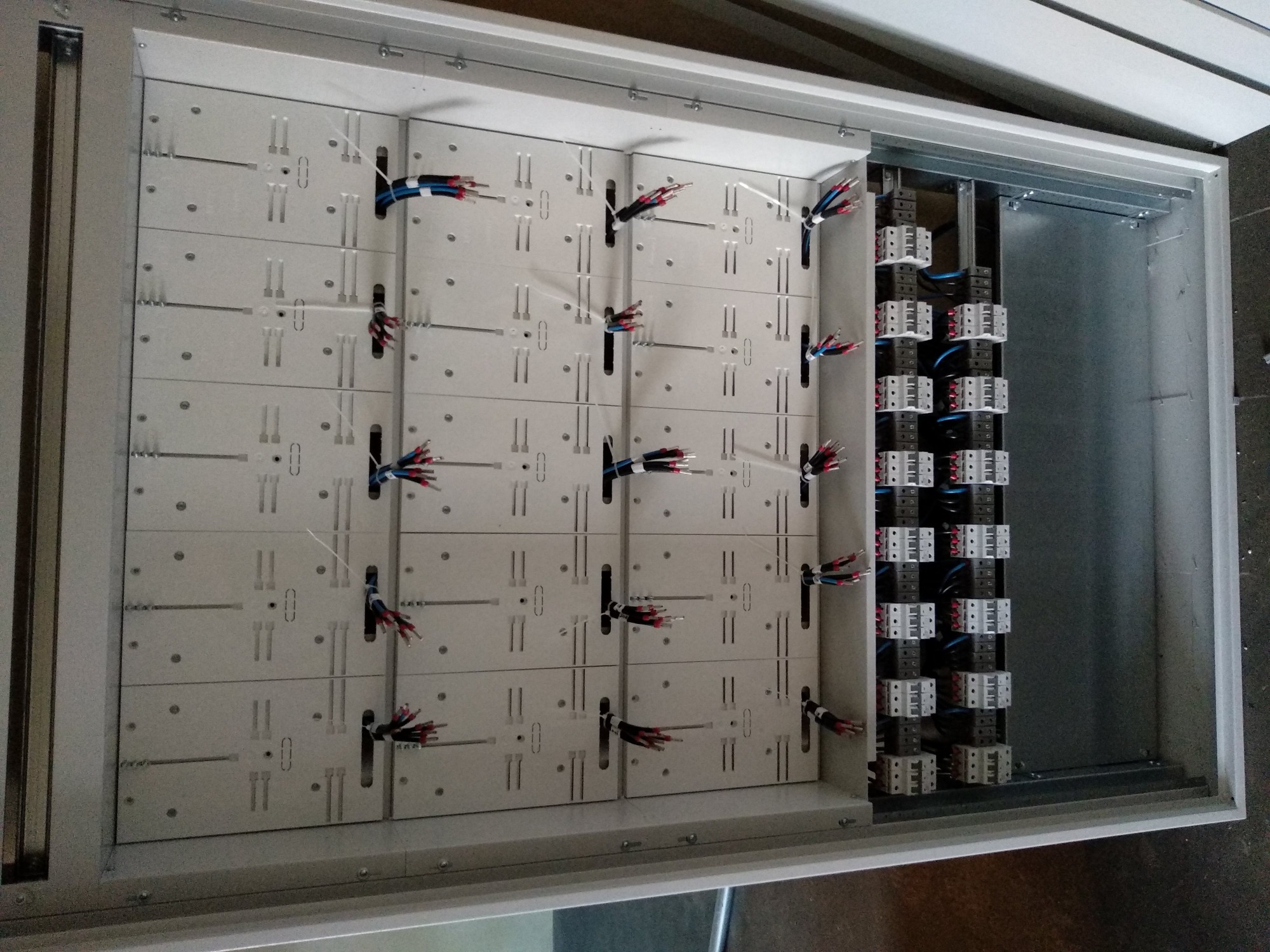 Wnętrze metalowej skrzynki rozdzielczej z zamontowanymi modułami i podłączonymi przewodami elektrycznymi, widoczne liczne złącza i kable w różnych kolorach.
