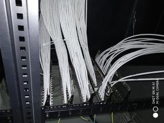 Rząd białych kabli sieciowych uporządkowanych w szafie rack, widok z dołu, ciemne tło, metalowa konstrukcja szafy po lewej stronie.