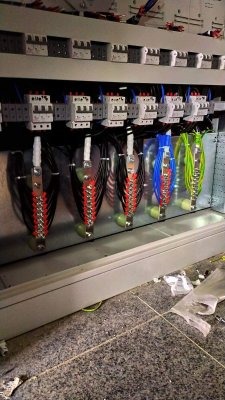 Rozdzielnica elektryczna w trakcie montażu, widoczne zabezpieczenia nadprądowe, listwy zaciskowe z podłączonymi przewodami w różnych kolorach oraz fragmenty izolacji na podłodze.