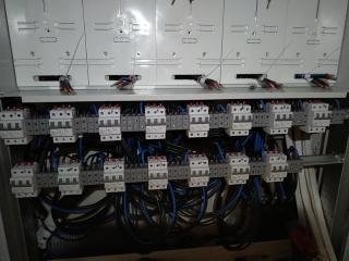 Rozdzielnica elektryczna z zamontowanymi bezpiecznikami i okablowaniem, widoczne szyny DIN i przewody w kolorze niebieskim, ułożone w regularny sposób.