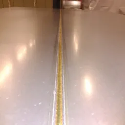 Widok z bliska na świeżo wykonane spawanie metalowych płyt, z widocznym złotym szwem spawalniczym i refleksami światła.