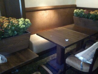 Tapicerowana brązowa ławka narożna z wysokim oparciem w restauracji, uzupełniona drewnianym stołem i donicami z kwiatami.
