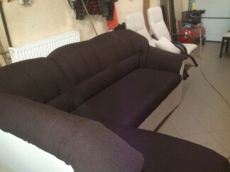 Ciemnobrązowa sofa z jasnymi bokami w pomieszczeniu warsztatowym, widoczny kompresor i krzesła w tle.