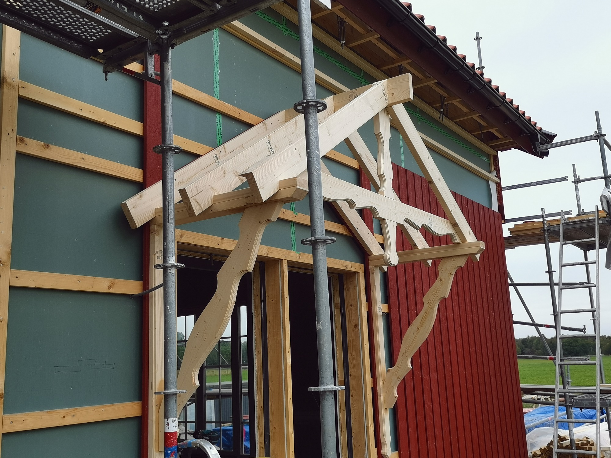 Budowa zadaszenia nad wejściem do budynku, widoczne drewniane elementy konstrukcyjne i rusztowanie.