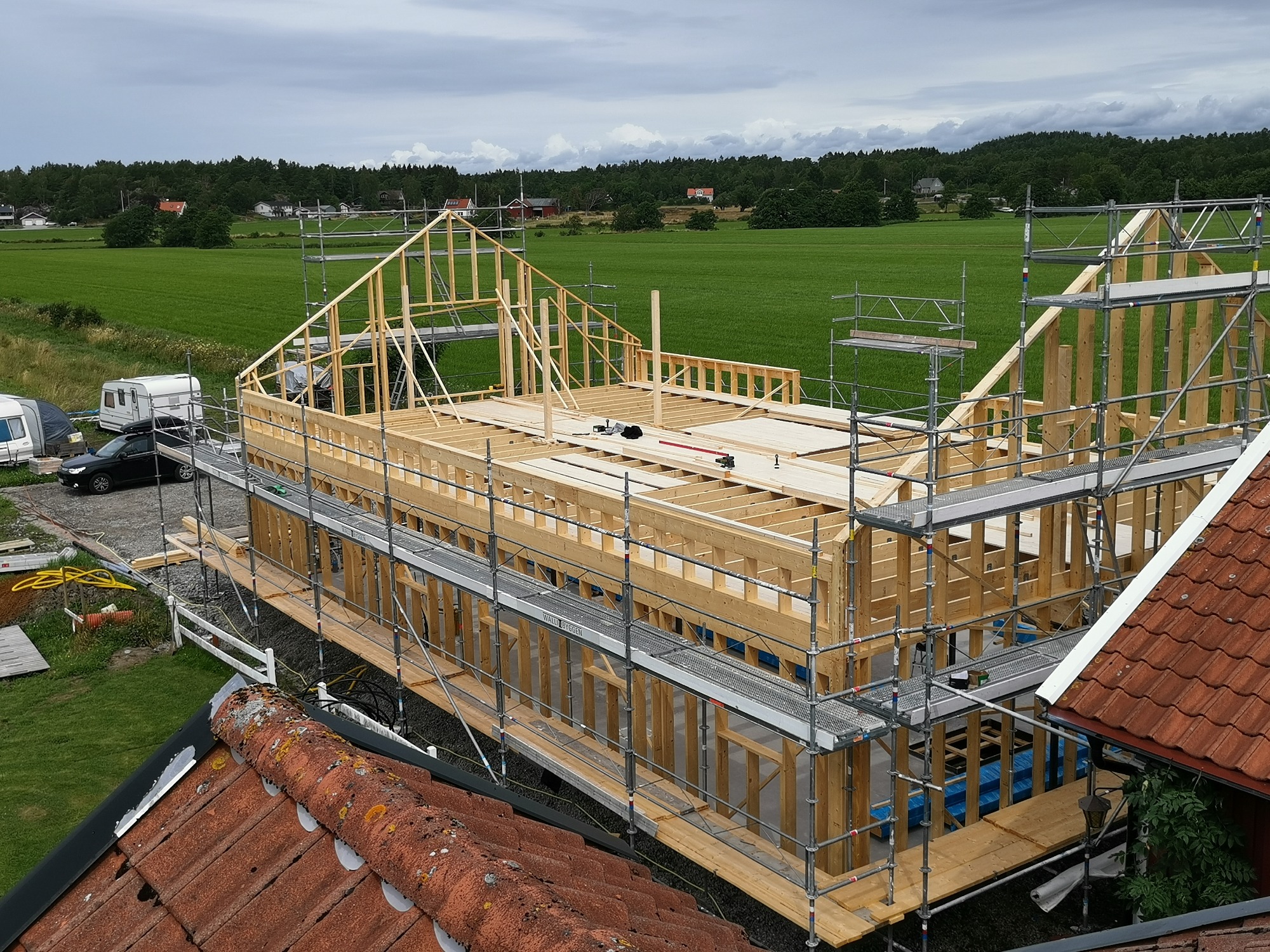 Konstrukcja drewniana nowego dachu w trakcie budowy, widok z góry na rusztowania i okoliczne pola w pochmurny dzień.