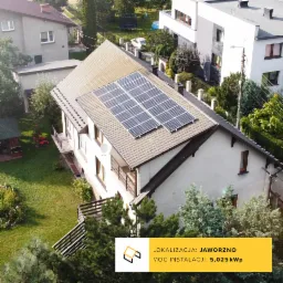 Dom jednorodzinny z brązowym dachem, na którym zamontowano panele słoneczne w układzie 2x4, widok z góry, w tle zabudowa jednorodzinna i zieleń.