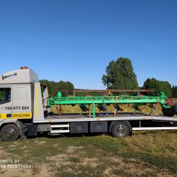 Pomoc drogowa Goleniów - Laweta przewozi zielony agregat uprawowy na tle łąki i lasu w słoneczny dzień.