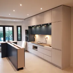 Nowoczesna kuchnia w trakcie montażu, z szarymi szafkami, czarnymi akcentami i wyspą bez blatu, widoczne niedokończone podłączenia elektryczne.