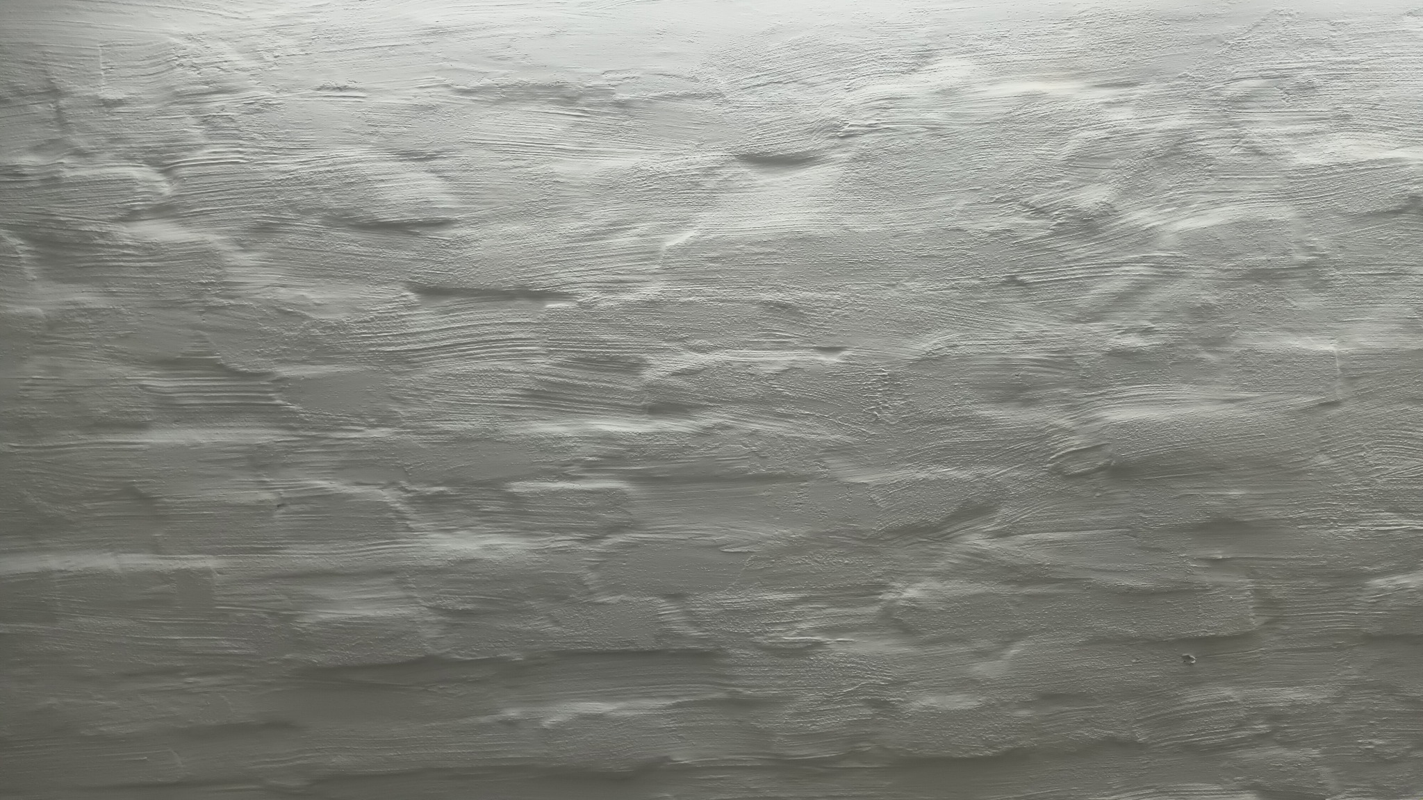 Szara ściana z wyraźną, fakturowaną strukturą, imitująca cegły, z widocznymi śladami pędzla i nierównościami w nałożeniu farby.