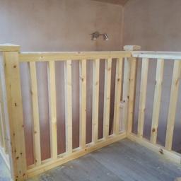 Dobra robota. - Surowa drewniana balustrada schodowa z prostymi szczeblami, zamontowana w rogu pokoju z surowymi ścianami i podwójnym reflektorem sufitowym.