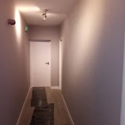 Korytarz w trakcie malowania w Tomaszowie Mazowieckim, zabezpieczona podłoga, świeżo pomalowane szare ściany, białe drzwi.