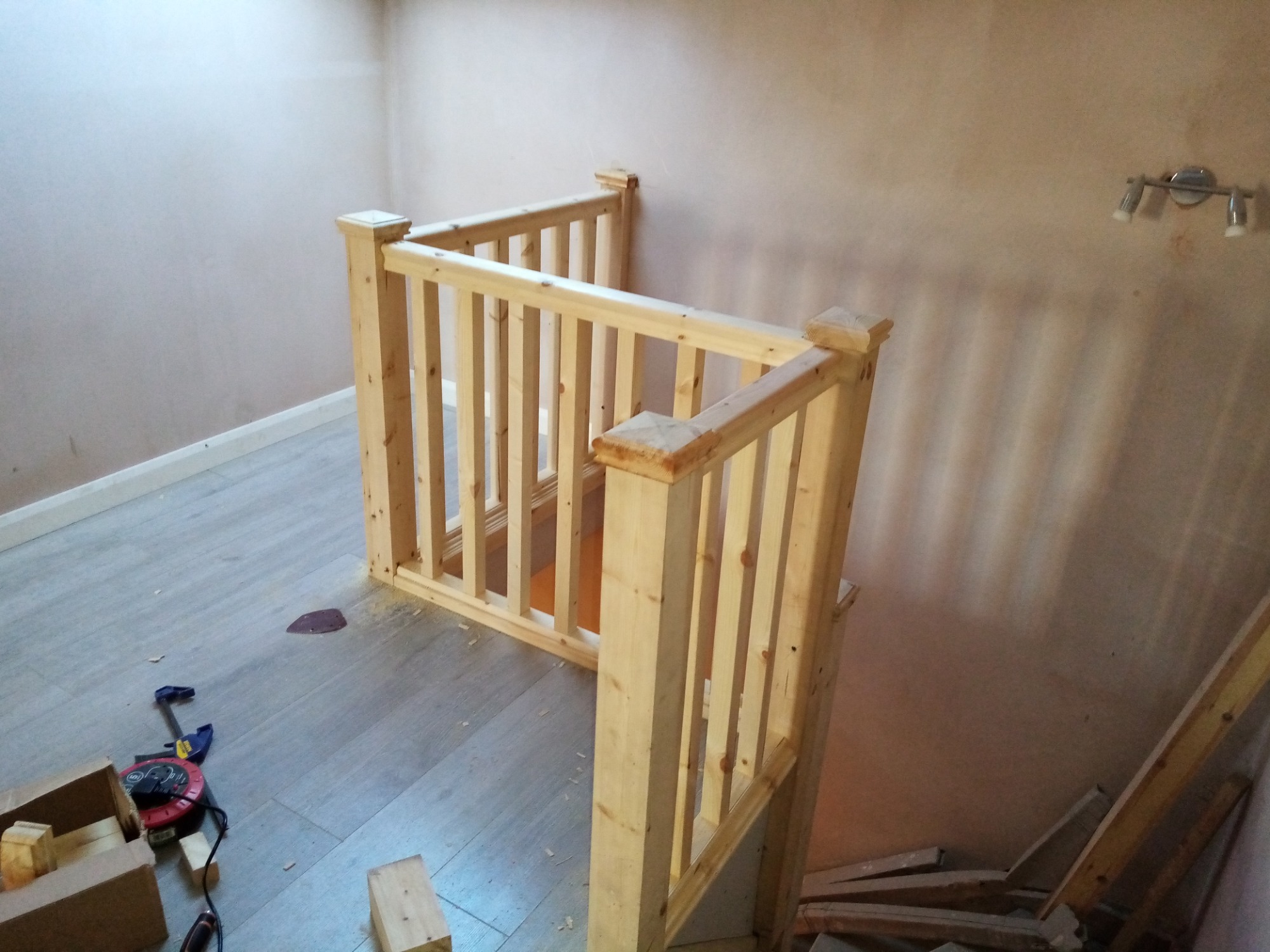 Montaż drewnianej balustrady schodowej na antresoli, widoczne narzędzia i resztki drewna na podłodze.